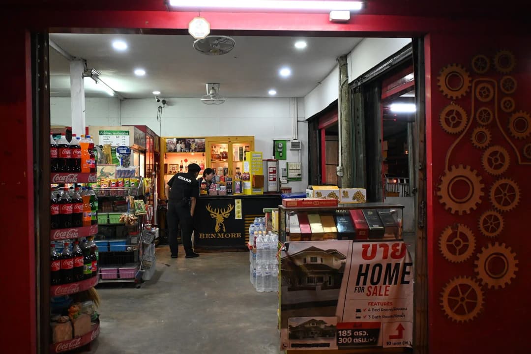 This photo shows a small convenience store or minimart viewed from the outside, looking in through the entrance. Inside, there's a brightly lit shop with various merchandise displayed on shelves. Ther